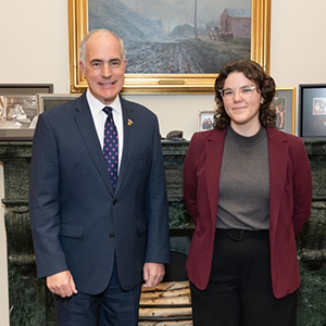 A young woman with dark hair wearing a dark blazer poses with US Senator Bob Casey in his office.