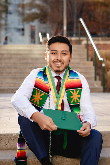 Jason Mercado sits on the steps of the Johnson Center with his stoll, Honors medal, and graduation cap.